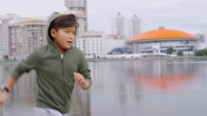 年轻的亚洲男孩沿着城市河边人行道慢跑