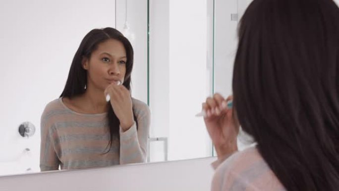 女人看着浴室镜子里的倒影刷牙