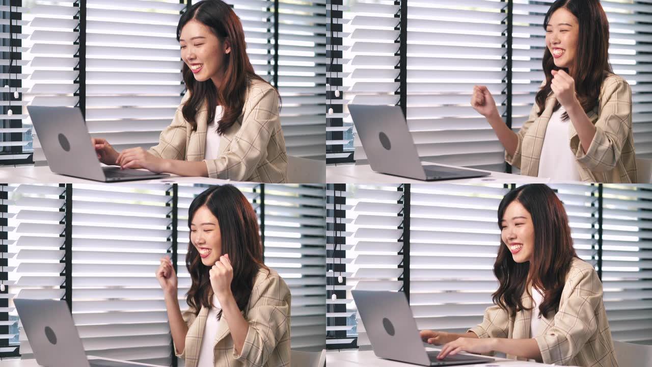 兴奋的女商人坐在办公桌前，在笔记本电脑上读好消息，这是亚洲女商人的快乐写照。成功快乐的女人庆祝