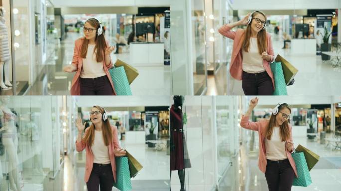 快乐女人戴着耳机享受音乐，拿着纸袋在商场大厅里跳舞唱歌。女孩在商店橱窗里看着衣服，玩得开心。