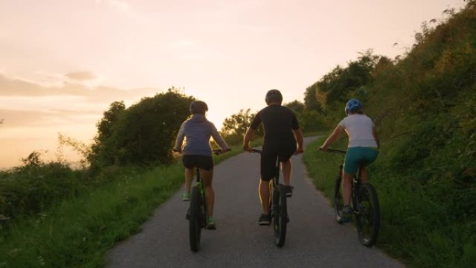 镜头耀斑: 无法识别的骑自行车的人在金色日落时沿着空旷的道路踩踏板。