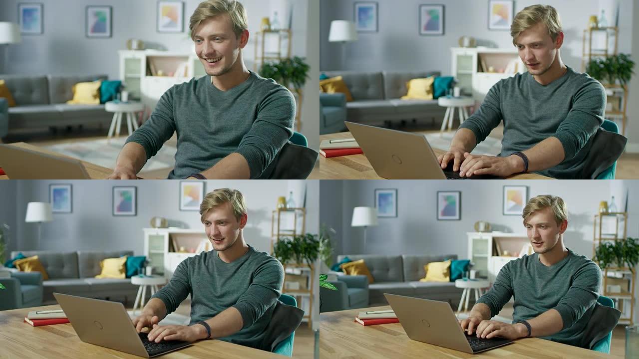 英俊的微笑的年轻人坐在舒适的客厅的桌子旁使用笔记本电脑。