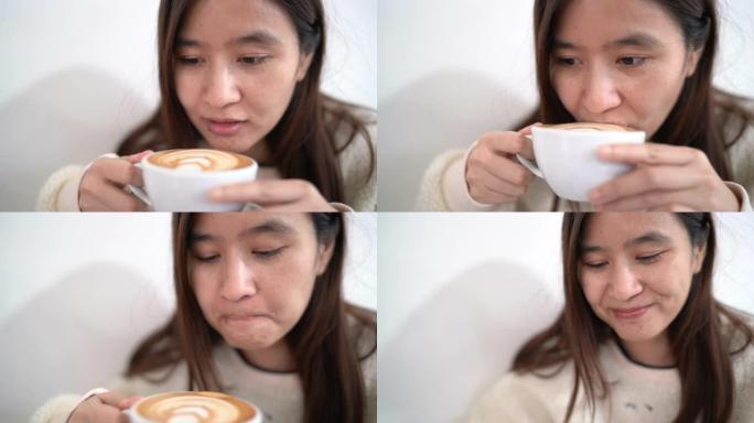 亚洲年轻女子在冬天在咖啡馆里拿着和喝热拿铁咖啡