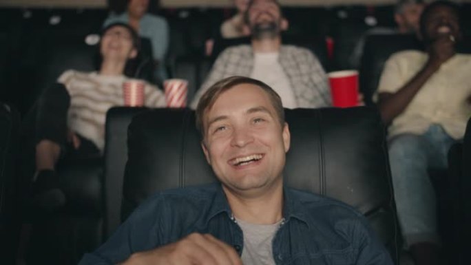 快乐的家伙笑着吃爆米花指着电影院看电影