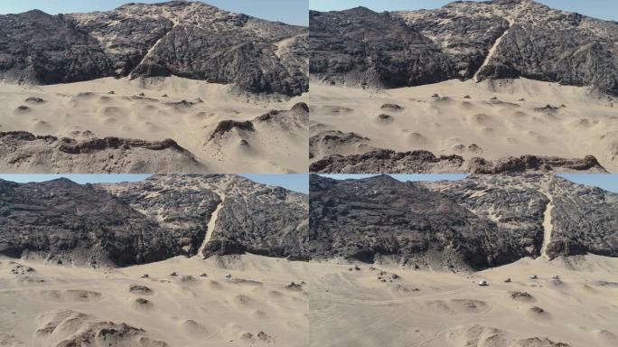 纳米比亚纳米布沙漠骨架海岸上4x4车辆车队在沙丘和山脉之间行驶的4k空中平移视图