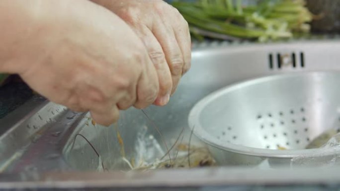 亚洲高级妻子在家里的厨房里为晚餐洗新鲜虾