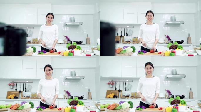 年轻的亚洲女性影响者vlogger穿着白色西装，在厨房对着镜头微笑。相机放大