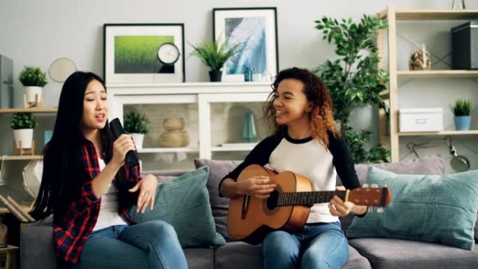 女性朋友在家里玩得开心，在电视遥控器里弹吉他唱歌，一起享受家里的休闲活动。音乐和文化概念。