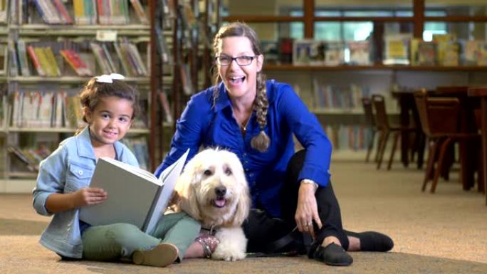 西班牙裔女孩与治疗犬一起在图书馆读书