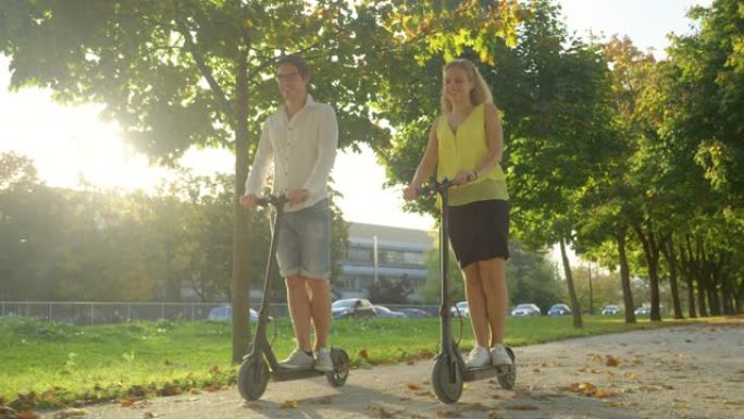 镜头耀斑: 微笑的高加索夫妇在充满活力的大街上骑着电动踏板车