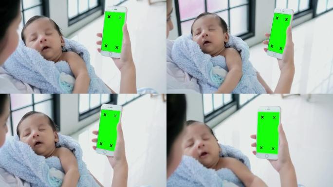 母亲抱着孩子时使用智能手机 (绿屏)。