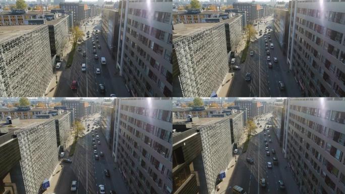 空中无人机镜头在汽车交通适中的城市街道上方飞行。晴天在两排办公楼之间的街道上。