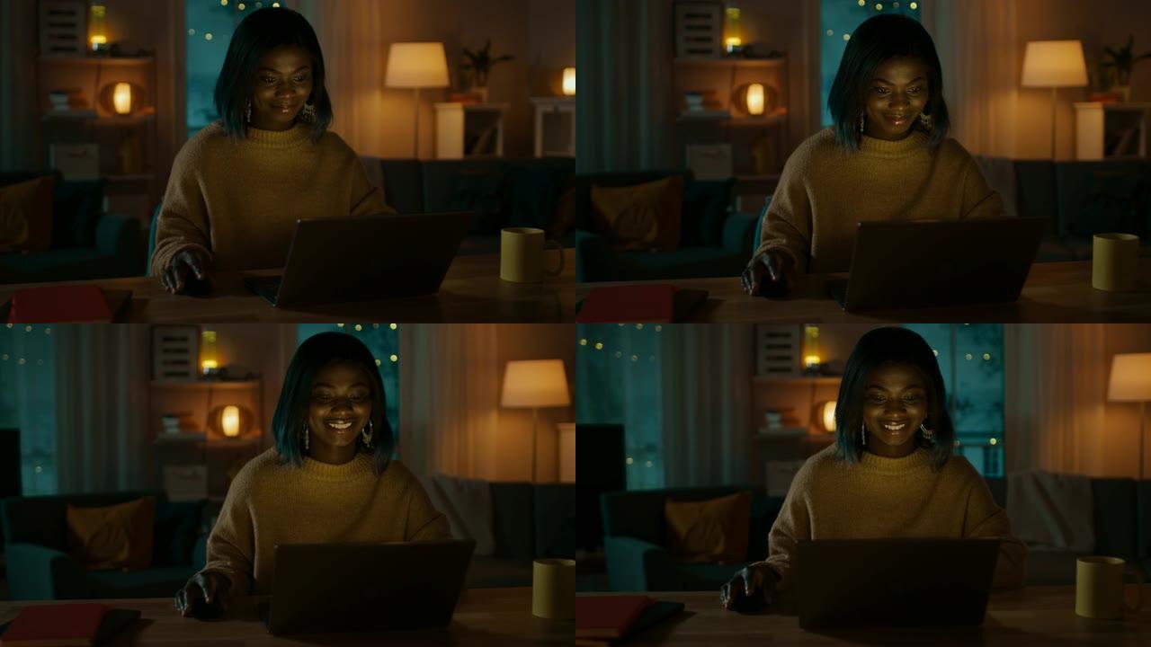 美丽微笑的非洲裔美国女孩坐在家里的办公桌前使用笔记本电脑的肖像。晚上，有创意的女人在舒适的客厅里用电