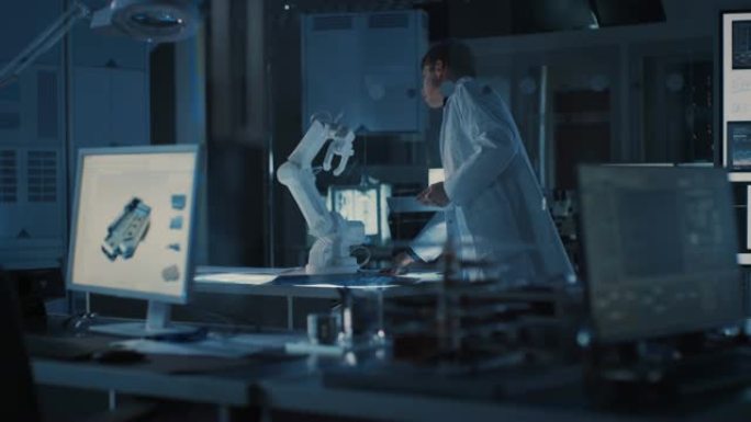 专业的重工业机器人工程师穿着白色外套拿着平板电脑走过实验室。设施充满计算机，各种工业设计组件和机械臂