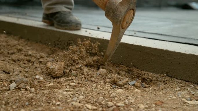 特写: 无法识别的工人使用镐开始挖掘砾石地面