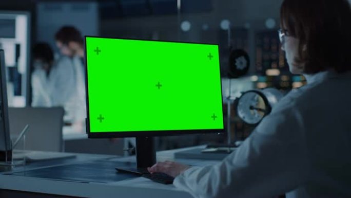 肩膀上的镜头: 女IT科学家使用绿色模拟屏幕计算机。在背景技术研究与开发实验室中，科学家，从事高科技