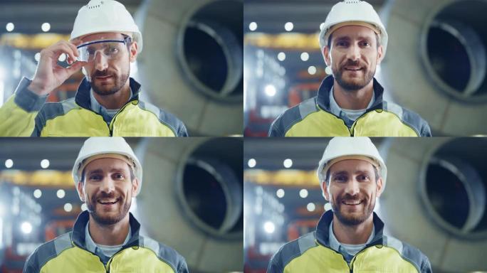 微笑的专业重工业工程师/工人穿着安全制服和安全帽的肖像。在背景中没有聚焦的大型工业工厂