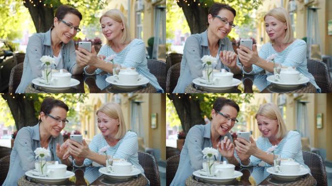 兴奋的女性在城市街道的露天咖啡馆里使用智能手机大笑