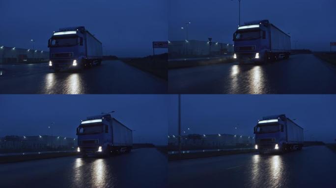 满载货物拖车的长途半卡车在夜间在高速公路上行驶，穿过雨、雾、雪穿越大陆。工业仓库区。正面跟随镜头