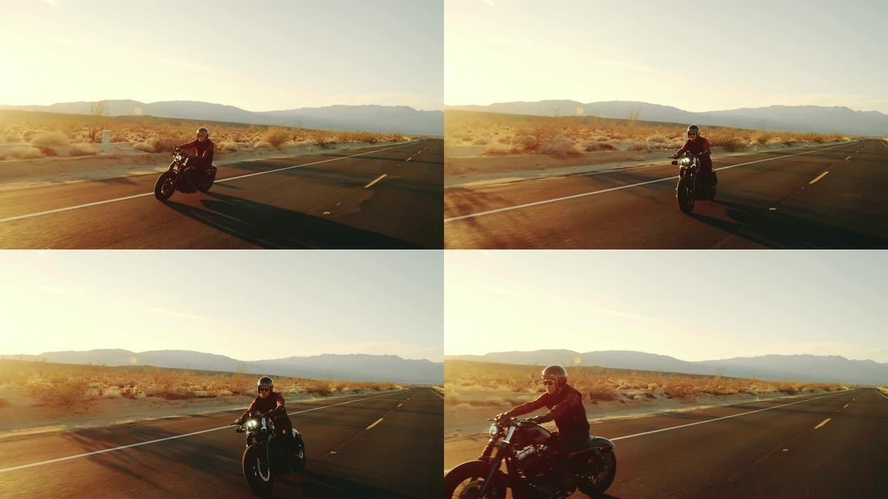 快乐的人骑着老式黑色摩托车在日落时沿着沙漠高速公路行驶