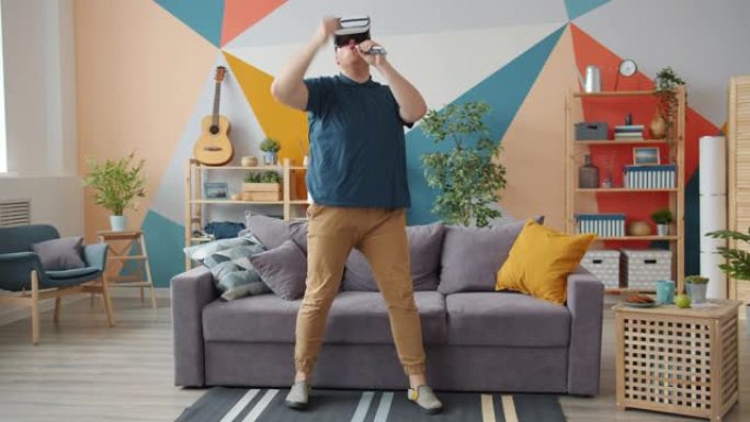 有创意的男人在家中戴着虚拟现实眼镜在遥控器中唱歌