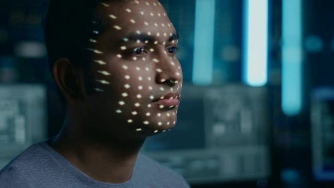 英俊的年轻印度男子通过生物识别面部识别扫描过程进行识别。未来派概念: 投影仪通过点照明面部并用激光扫