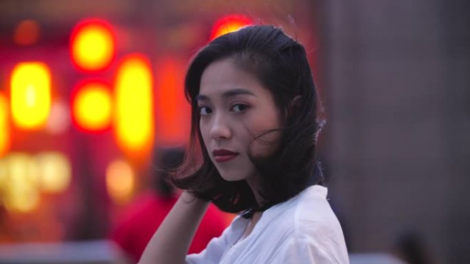 迷人的年轻亚洲女子在城市夜晚对着镜头微笑