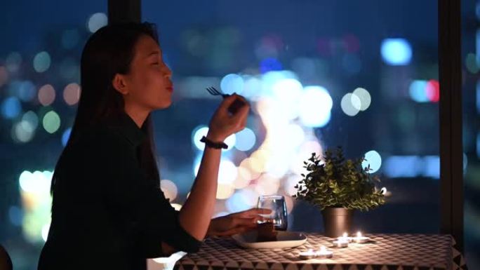 一位亚洲中国美丽的年轻女士在神奇的时刻，黄昏放松和享受的时刻在她的公寓里吃甜点