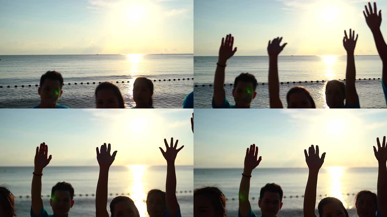 快乐的志愿者站在沙滩上举手，团结协作的理念。