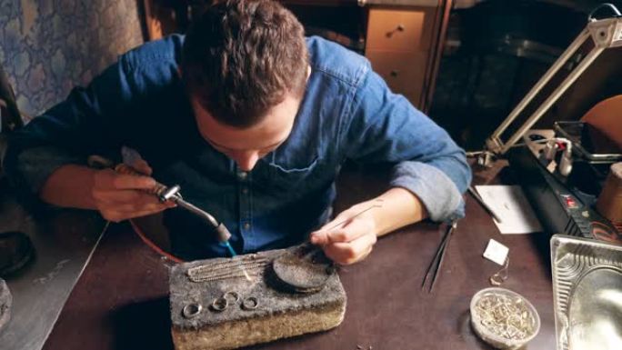 男性珠宝商使用燃烧器焊接银链。