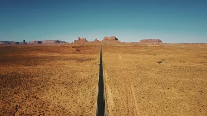 无人驾驶飞机在亚利桑那州纪念碑谷空旷的砂岩沙漠公路上方向后飞行，山峦平坦。