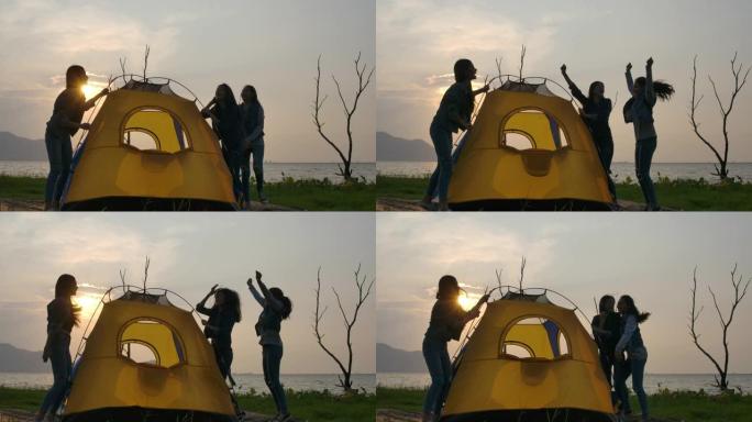 慢动作 -- 年轻的亚洲女孩在夏天的湖边搭起帐篷的剪影。露营、旅行和友谊概念。