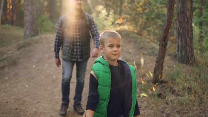 快乐的孩子和他的父亲在野生森林徒步旅行的慢动作，微笑着享受户外活动和自然。童年，热爱家庭和旅游理念。