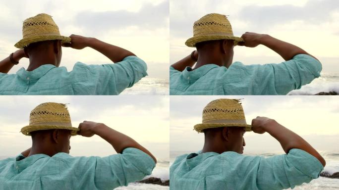戴着帽子的非洲裔美国人站在海滩上的后视图4k