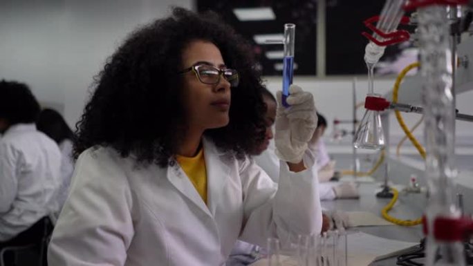 漂亮的黑人学生在化学课上在记事本上做笔记时非常近距离地看着试管中的液体