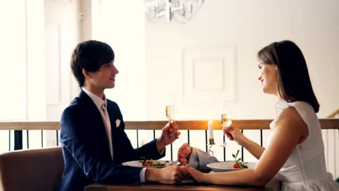可爱的情侣女孩和男孩在餐厅浪漫约会时拿着酒杯边说边笑。快乐的青春，浪漫和饮料的概念。