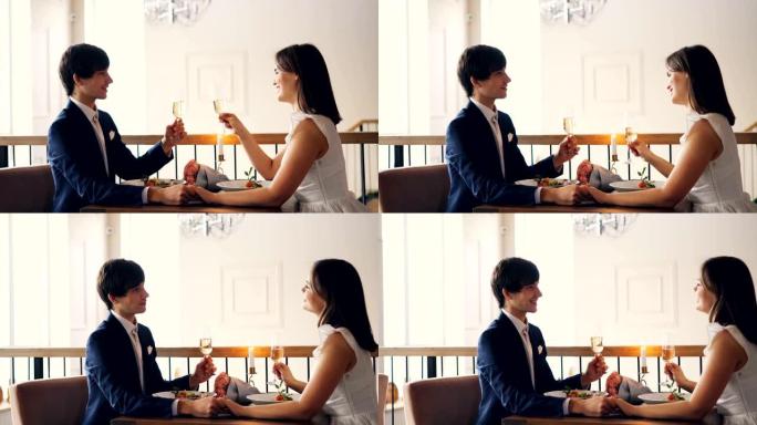 可爱的情侣女孩和男孩在餐厅浪漫约会时拿着酒杯边说边笑。快乐的青春，浪漫和饮料的概念。