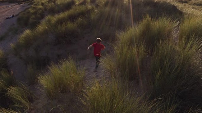 在沙滩度假中，小男孩在沙丘上对着烈日玩耍的无人机拍摄