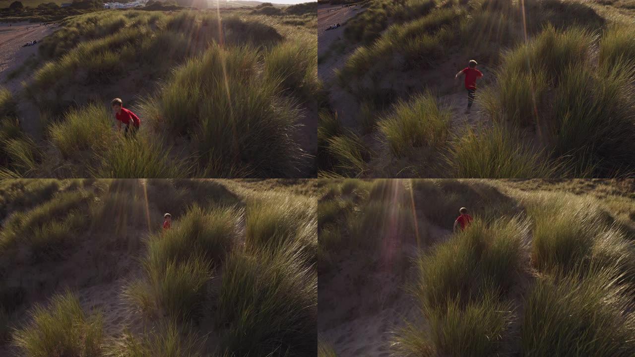 在沙滩度假中，小男孩在沙丘上对着烈日玩耍的无人机拍摄