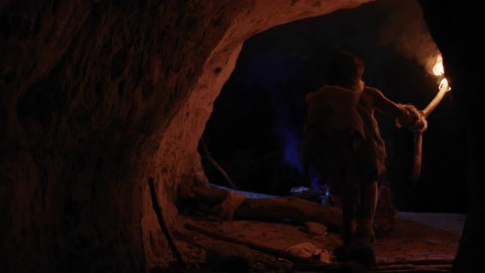 原始穴居人穿着动物皮在夜间探索洞穴，拿着火把看着夜晚在墙上的图画尼安德特人寻找安全的过夜场所。后视图