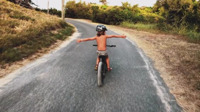 无忧无虑的男孩骑着自行车，双臂伸出