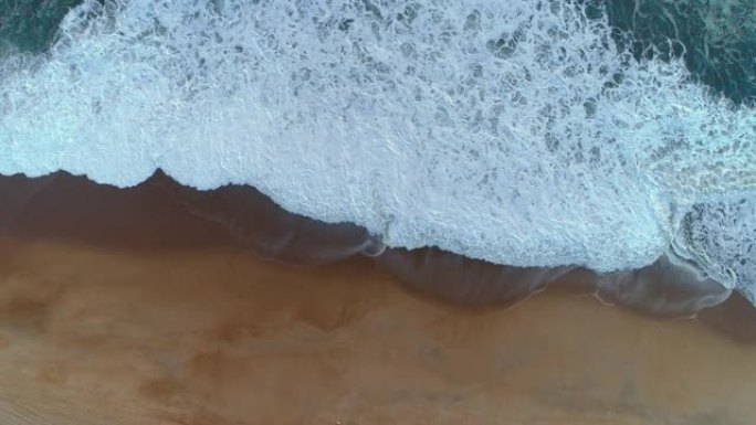 沙滩上冒出泡沫的波浪。葡萄牙大西洋沿岸。空中自上而下拍摄，4K