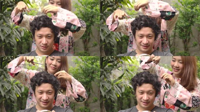 年轻的亚洲女性试图在家里用剪刀给她的男朋友或丈夫理发，因为被封锁了。居家隔离冠状病毒大流行预防，社会