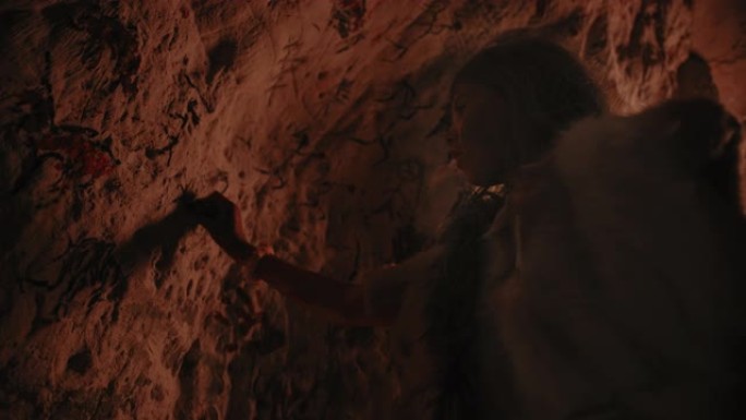 原始的史前尼安德特人的孩子穿着动物皮在晚上在墙上画动物和摘要。用岩画创造第一个洞穴艺术，用火照亮的岩