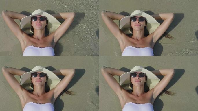 一个美丽的年轻女子在海上晒日光浴的肖像，穿着泳衣，白色草帽，海沙背景。