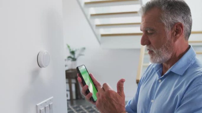 资深西班牙裔男子在家里使用手机应用程序控制数字中央供暖恒温器