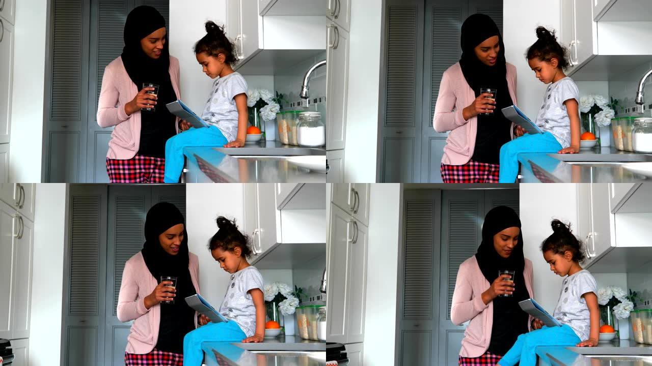 带着头巾的年轻母亲在厨房4k的女儿附近喝了一杯水