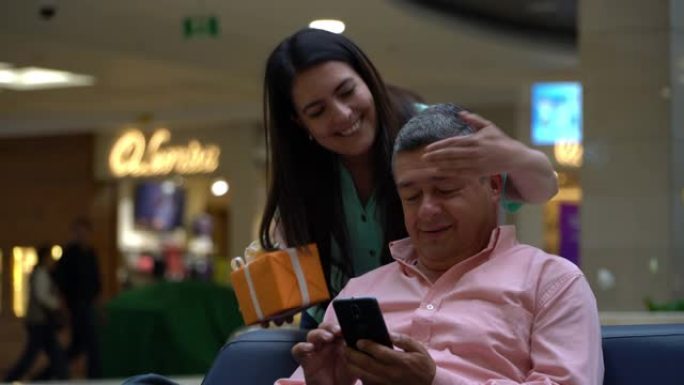 开朗的成年女性令人惊讶的伴侣正在购物中心的智能手机上与礼物聊天