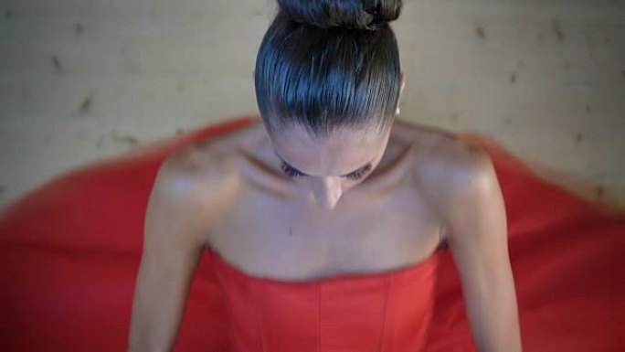 一位美丽的轻型芭蕾舞演员的肖像，穿着一件郁郁葱葱的红色连衣裙，坐在木地板上，灵活，俯视图。