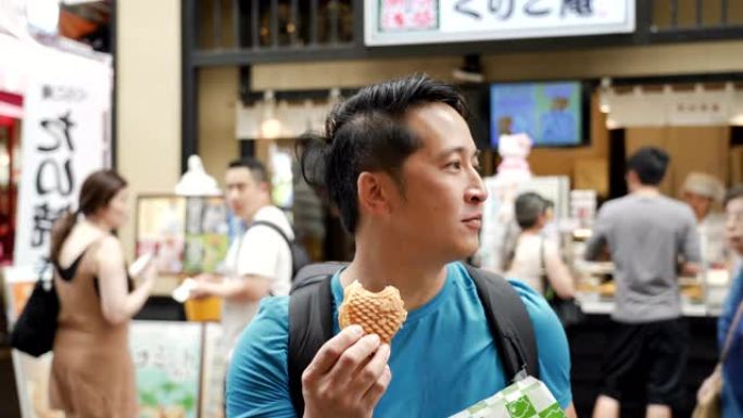 亚洲男子在街头食品市场吃Taiyaki